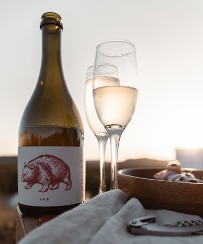 Premium organic wine bottle and flutes on a wooden table at sunset, with cured meats and vineyard view